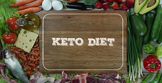 keto fasting diet white letters written on a wooden cutting board and surrounded by some vegetables fruits lean meats eggs olive oil and cheese